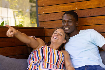 A diverse couple relaxes together, the woman pointing at something in the distance