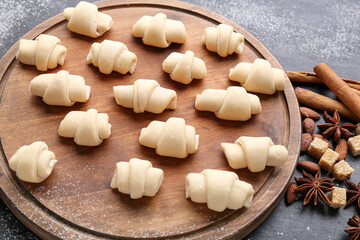 Wooden board with raw croissants and spices on dark background, closeup