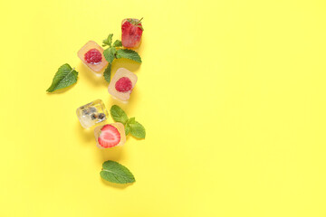 Frozen berries in ice cubes and mint on yellow background