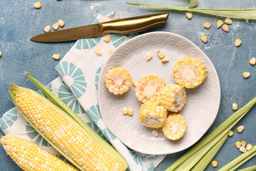Plate with cut fresh corn cob and seeds on blue background