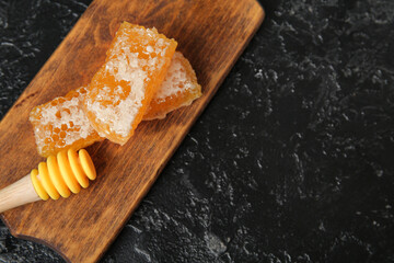 Wooden board with sweet honeycombs and dipper on dark background