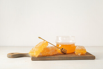 Wooden board with jar of tasty honey and combs on light background