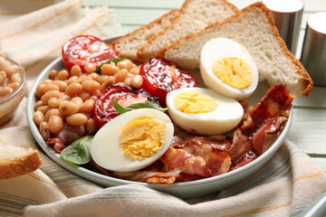 Plate of tasty English breakfast with boiled eggs on green wooden background