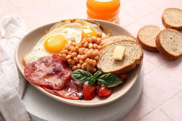 Plate of tasty English breakfast with fried eggs on pink tile background