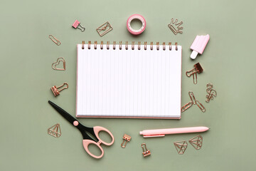 Notebook with different stationery supplies on green background
