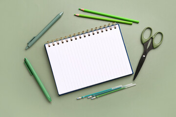 Notebook with different stationery supplies on green background