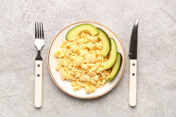 Plate of tasty scrambled eggs with avocado on grey background