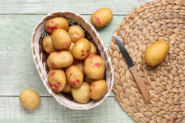 Wicker bowl with fresh raw potatoes on green wooden background
