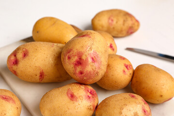 Board with fresh raw potatoes on white background