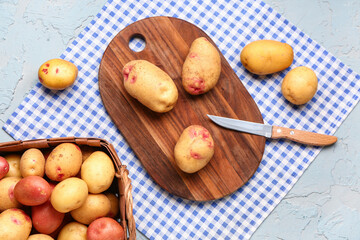 Wooden board and wicker basket with fresh raw potatoes on blue background