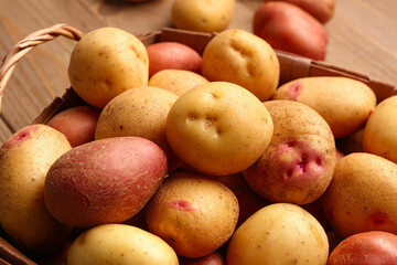 Wicker basket with fresh raw potatoes on wooden background, closeup
