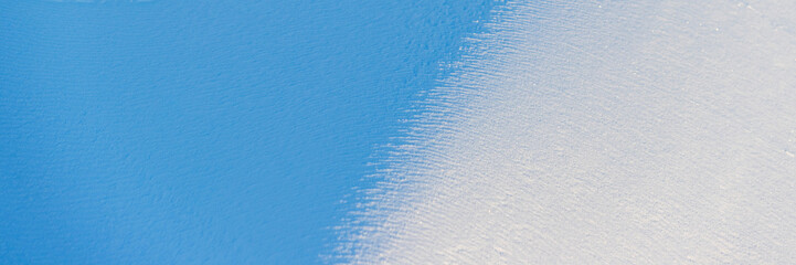 Beautiful winter background with snowy ground. Natural snow texture. Wind sculpted patterns on snow surface. Wide panoramic texture for background and design. Closeup top view with copy space.