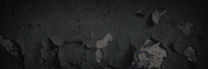 Dark wide panoramic background. Peeling paint on a concrete wall. Dark grunge texture of old cracked flaking paint. Weathered rough painted surface. Patterns of cracks. Darkness background for design.