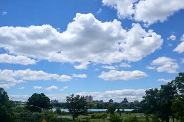Bright blue sky with soft fluffy clouds. A lake and trees in the foreground. 