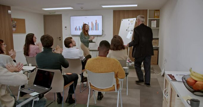 Multi ethnic team of employees in a modern classroom engages in a business meeting, showing appreciation with applause, reflecting a positive and collaborative work atmosphere.