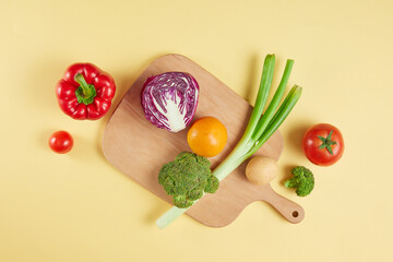 Photo for restaurant or cooking advertising with fruits and vegetables for healthy meal, a broccoli, cabbage, leek, potato and orange displayed on wooden chopping in center of yellow counter top