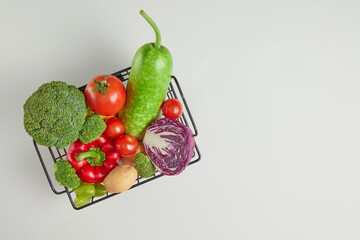 Top down photo with the black basket containing green broccoli, ripe tomato, green squash, potato and purple cabbage featured on white countertop. Space for product showing and designing