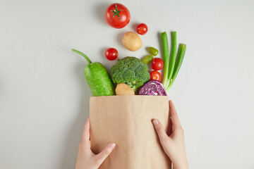 The photo shows a brown supermarket paper bag containing vegetables, held by two hands and dumped...