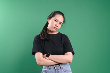 Portrait Of A Vexed Young Girl In Folded Arms Against Green Background