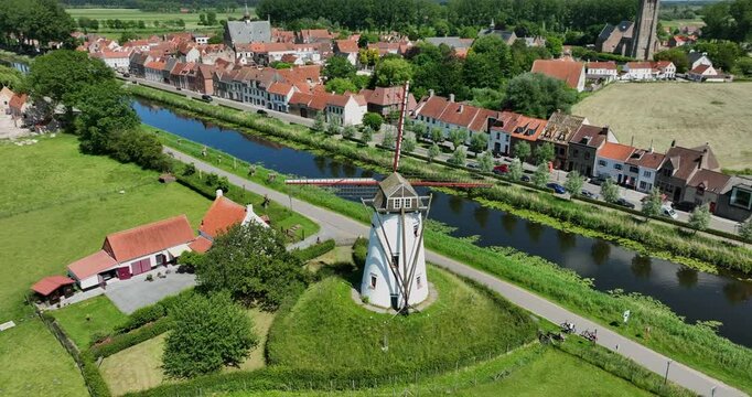 Damme, Belgium, June 2022. Drone orbits the Historic Schellemolen white windmill on a sunny day alongside the picturesque Damse Vaart canal.