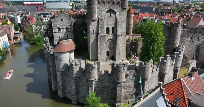 Gravensteen Castle, East Flanders, Ghent, Flemish Region, Belgium, June 2022. Drone pulls back revealing the iconic moat brick walls with flags waving proudly in wind over the city.