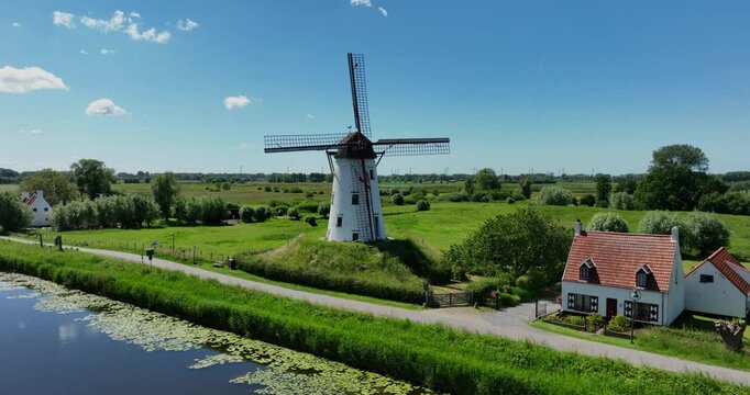 Damme, Belgium, June 2022. 
Drone orbits the Schellemolen a white windmill by the Damse Vaart a scenic canal on a sunny day.