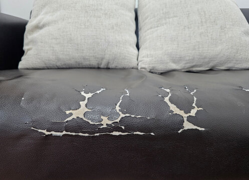 well worn black leather sofa with visible cracks and peeling, two grey cushions rest on the sofa