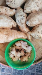 several sweet potatoes and galangal in a green container on a winnowing made of typical Indonesian woven bamboo called Nyiru