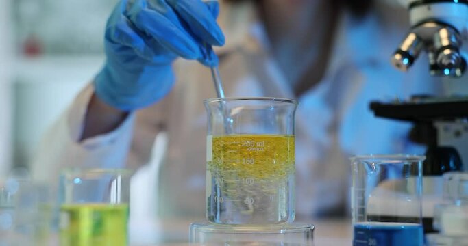 Scientist in gloves stirs substances in beaker at lab desk