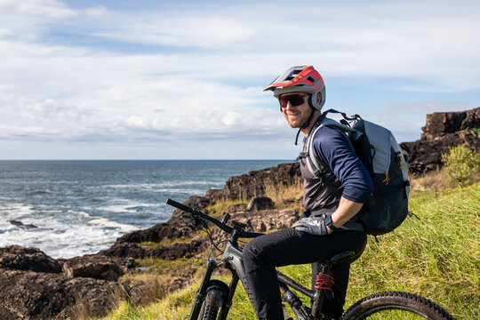 cacuasian man smile happy helmet mtb bie ride cycle bikepacking travel adventure cliff ocean sea water clouds gloves backpack