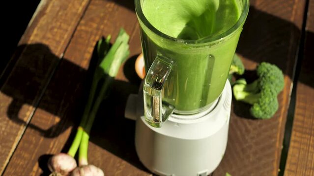The camera moves up over a blender mixing green smoothie from broccoli, spinach and avocado with garlic on a wooden brown table. Vegetarian smoothie made with raw green ingredients