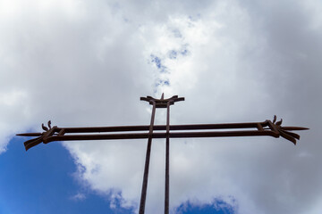rusty iron Christian cross seen from the ground with a blue sky with clouds in the background