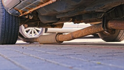 Broken Exhaust Pipe Muffler Laying on Ground Under Old Car with Rusty Undercarriage Chassis