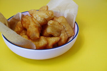 Deep-fried dough sticks or Patongko on a yellow background. Concept of deep frying, crispy texture, breakfast, and donut sticks. Asian cuisine dish of deep-fried dough sticks in a pink bowl.