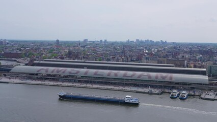 Aerial view of a tanker ship in Amsterdam's IJ river, passing the large Amsterdam sign with the cityscape in the distance, on a hazy spring day