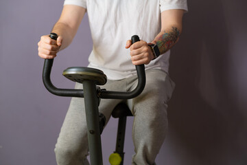 A close-up view of a mans hands gripping the handlebars of a stationary exercise bike. He is...