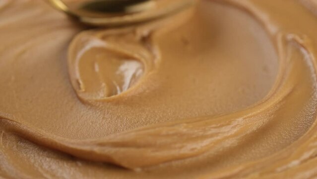 Peanut butter Mixing with golden spoon, close up. Creamy smooth peanut butter in jar. Organic food