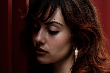 Low key portrait of young red hair woman leaning on red surface.