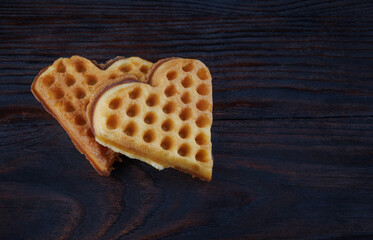 Two heart-shaped Viennese waffles lie on a dark wooden board.