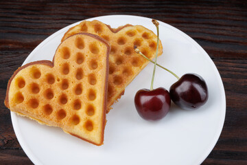 Viennese waffles with cherries lie on a white plate. Viennese waffles in the shape of a heart.