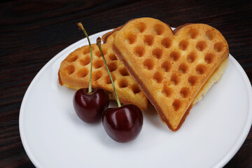 Viennese waffles with cherries lie on a white plate. Viennese waffles in the shape of a heart.