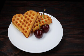 Viennese waffles with cherries lie on a white plate. Viennese waffles in the shape of a heart.