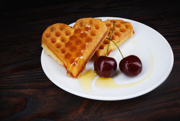 Viennese waffles with cherries lie on a white plate. Viennese waffles drizzled with honey in the shape of a heart.
