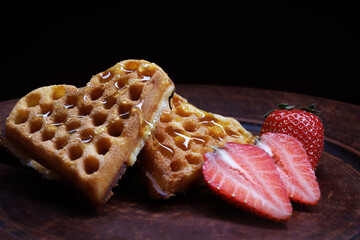 Viennese waffles drizzled with honey in the shape of a heart lie on a clay plate. Viennese waffles with cut strawberries.