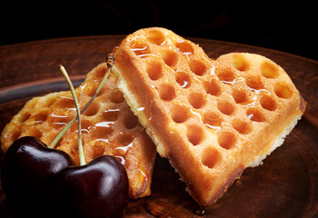 Heart-shaped Viennese waffles drizzled with honey lie on a clay plate. Viennese waffles with cherries.