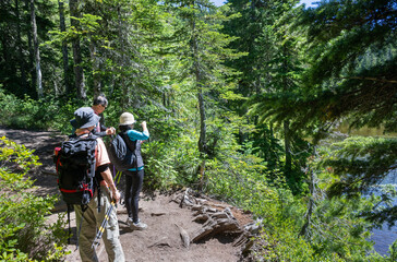 Three people hiking Summit Lake Trail, taking photos using smartphones. Mount Rainier National Park in summer. Washington State.