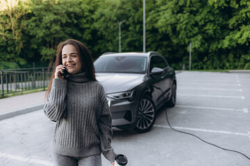 Fototapeta premium The beautiful successful European girl charges her electric SUV at the charging station in the city. Electric car, the means of transport of the future.