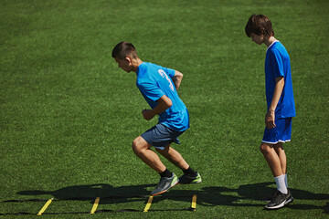 Agility Drill in Action. Two boys in blue jerseys concentrating on agility ladder drill, training, improving quickness and coordination. Concept of sport, school, childhood, hobby, active lifestyle