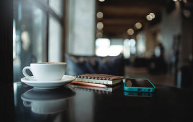 Comfortable workplace on table by the window in modern cafe with coffee drink and mobile phone, note book