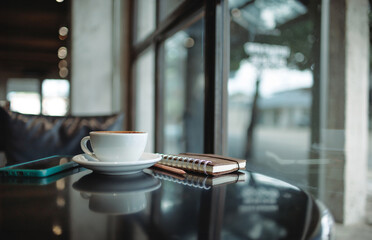 Comfortable workplace on table by the window in modern cafe with coffee drink and mobile phone, note book